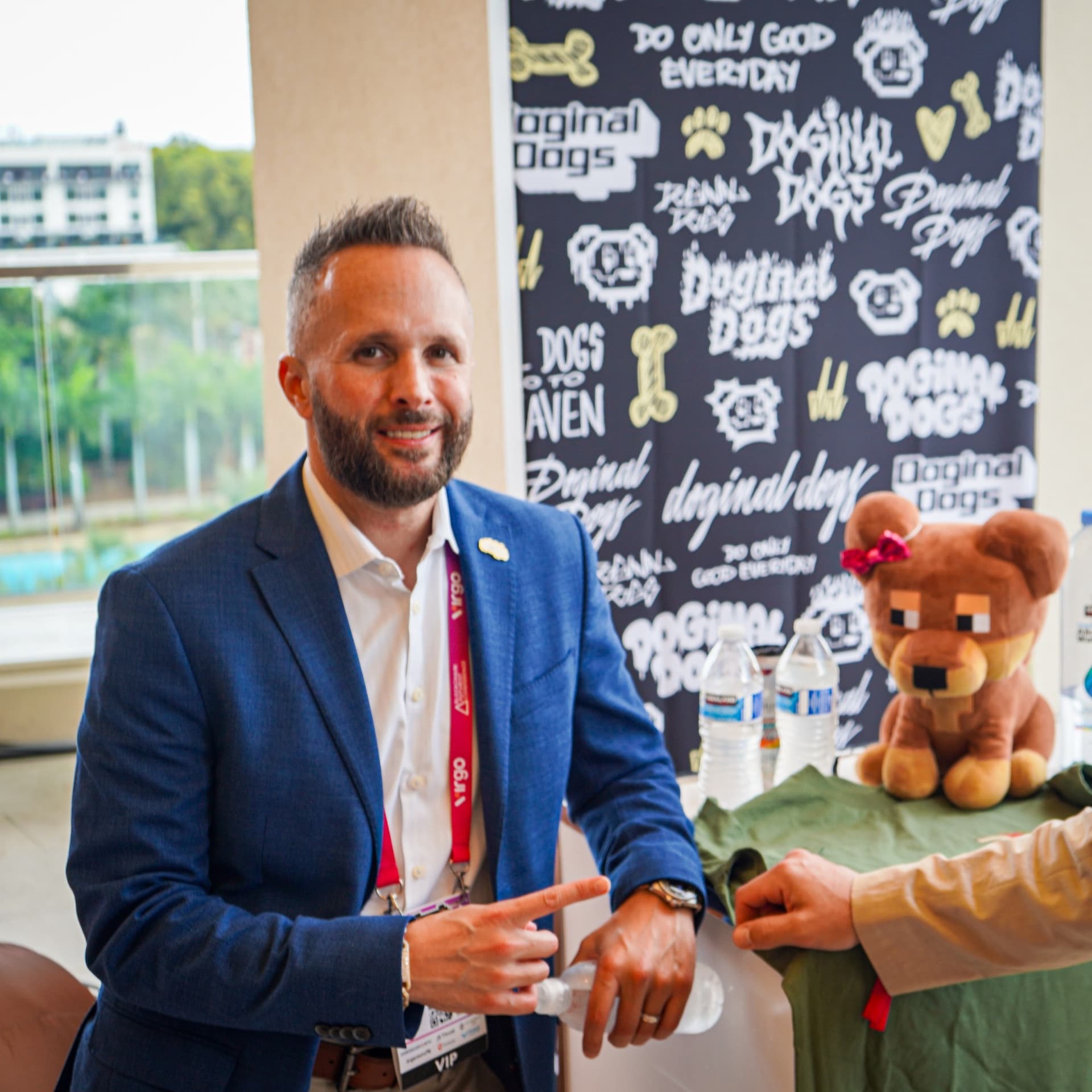 Damien Galvin — Shield at a Doginal Dogs table Damien Galvin, publicly known as Shield (@Shieldmetax), in a blue jacket at a Doginal Dogs table with a plush pixel dog
